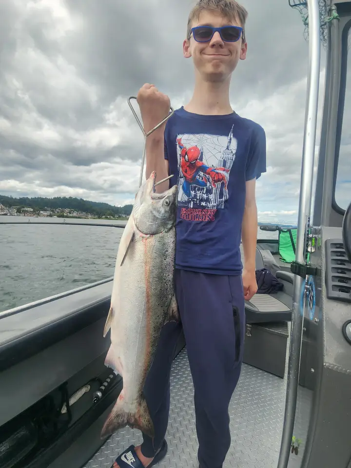 A boy in a Spiderman shirt holding a coho salmon