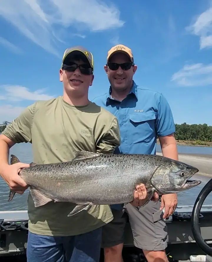 A teenage boy and his father with a big chinook salmon on a sunny day