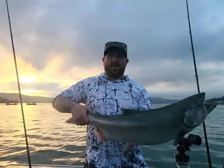 A bearded man holding a chinook salmon at sunrise