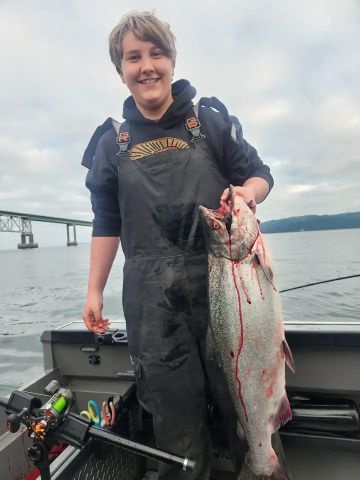 A teenage boy holding a chinook salmon with a bridge in the background