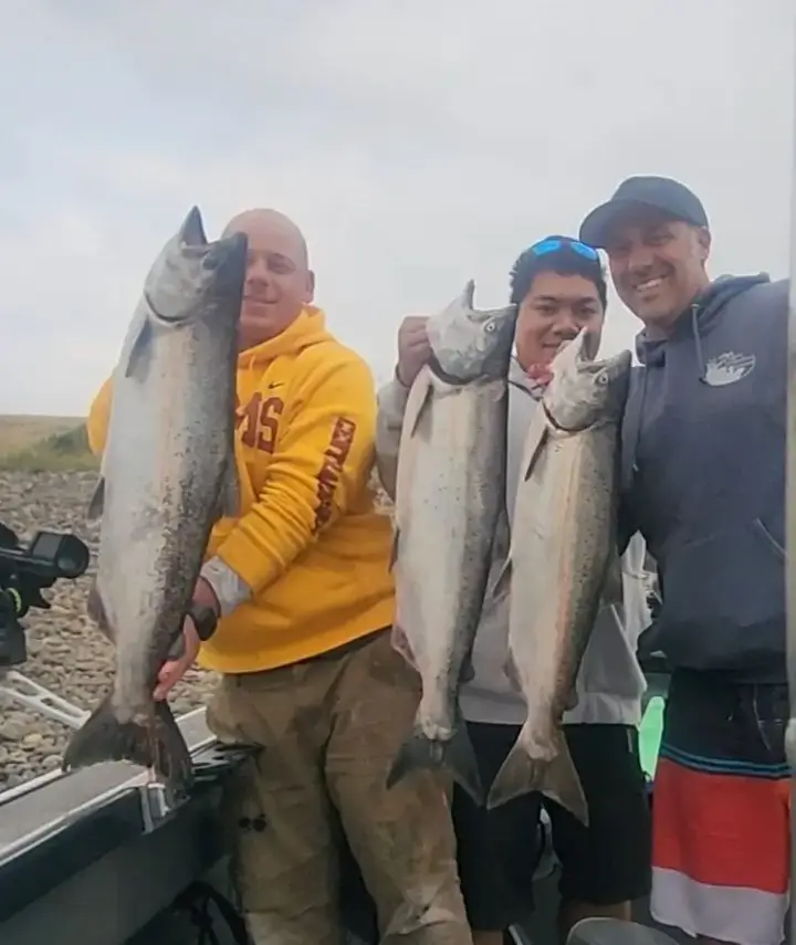 Three men on the boat holding salmon