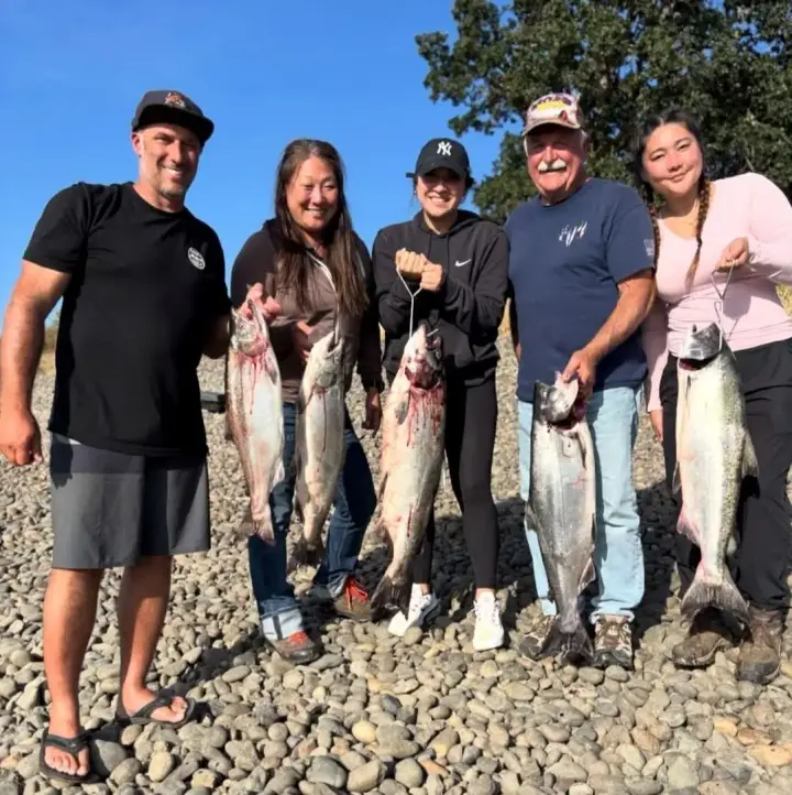 Five people on a rocky bank holding chinook salmon under a blue sky