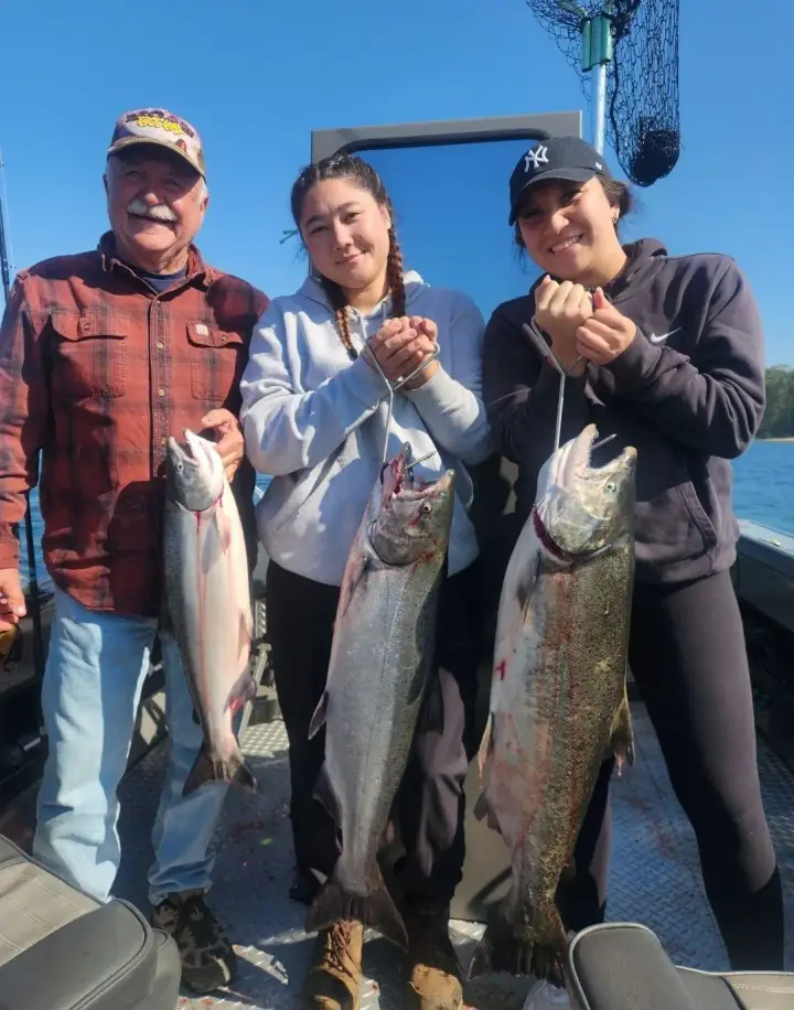 An older man and two young women holding three chinook salmon