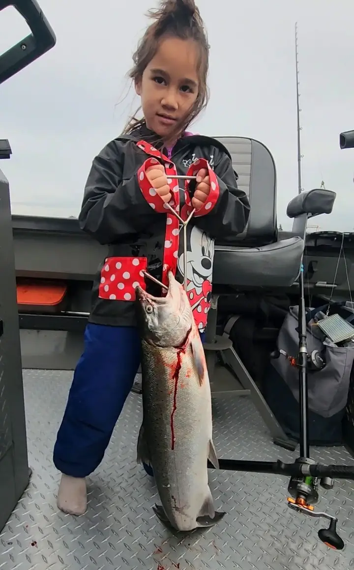A girl in a Minnie Mouse jacket holding a big coho salmon