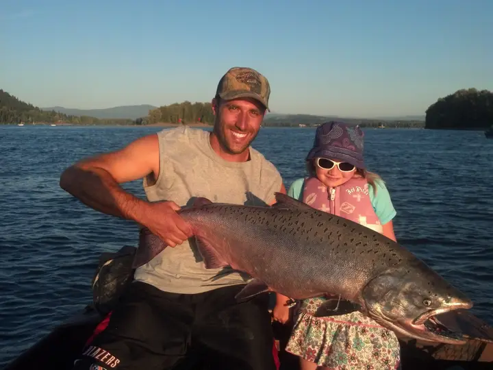 A man and a small girl in a sun hat holding a huge chinook salmon in golden light