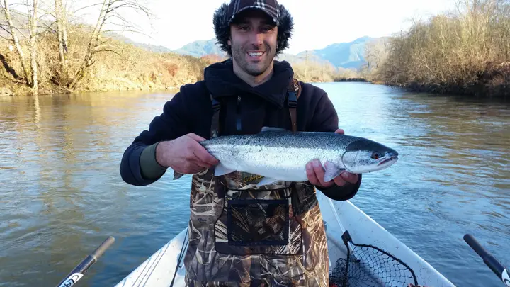 A man in a fur hat holding a steelhead from a drift boat in winter