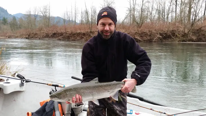 A man in a beanie holding a steelhead from a drift boat