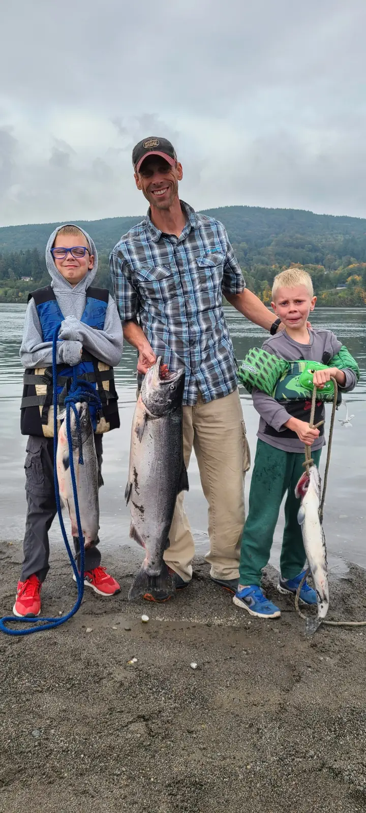 A father and two young sons on the beach holding three salmon