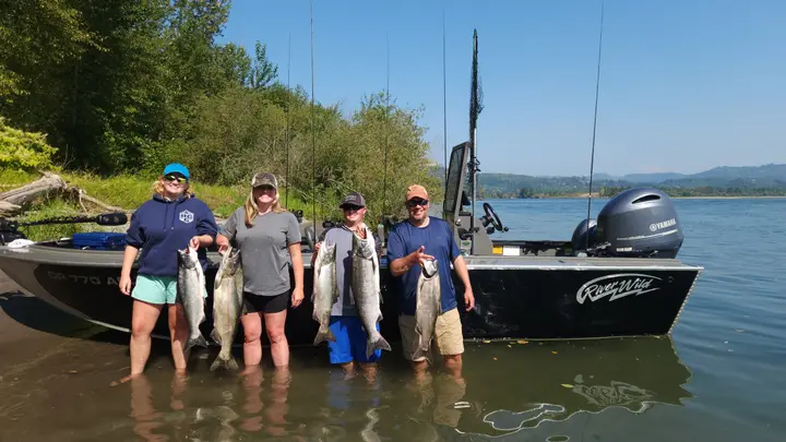 A family of four standing in the shallows beside the boat holding five salmon