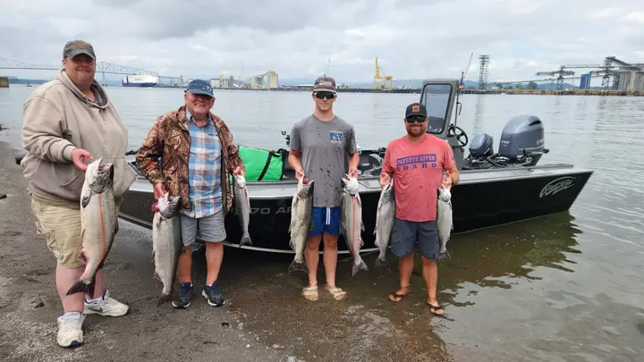Four men on the beach holding around ten salmon with the Astoria bridge behind
