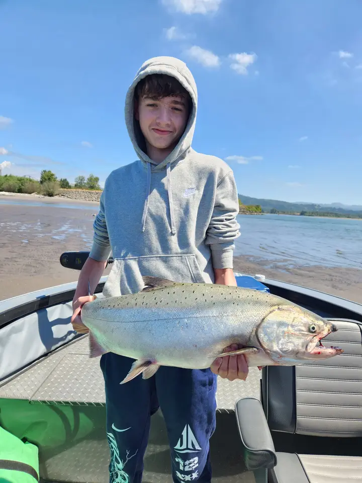 A teenage boy in a hoodie holding a large chinook salmon