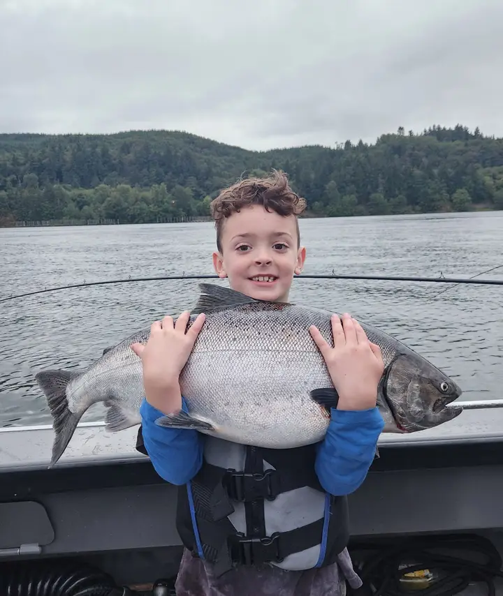 A boy in a life jacket hugging a large coho salmon aboard the boat