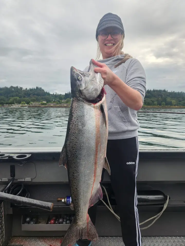 A woman in a beanie holding a large chinook salmon aboard the boat