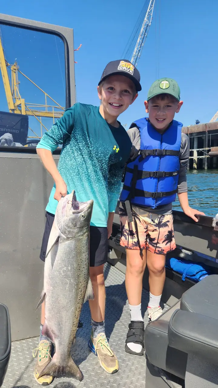 Two boys on the boat holding a chinook salmon with harbour cranes behind them