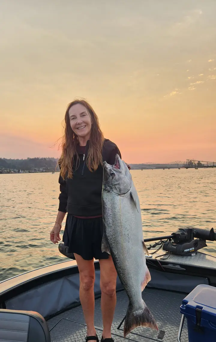 A woman holding a large chinook salmon at sunset on the Columbia River