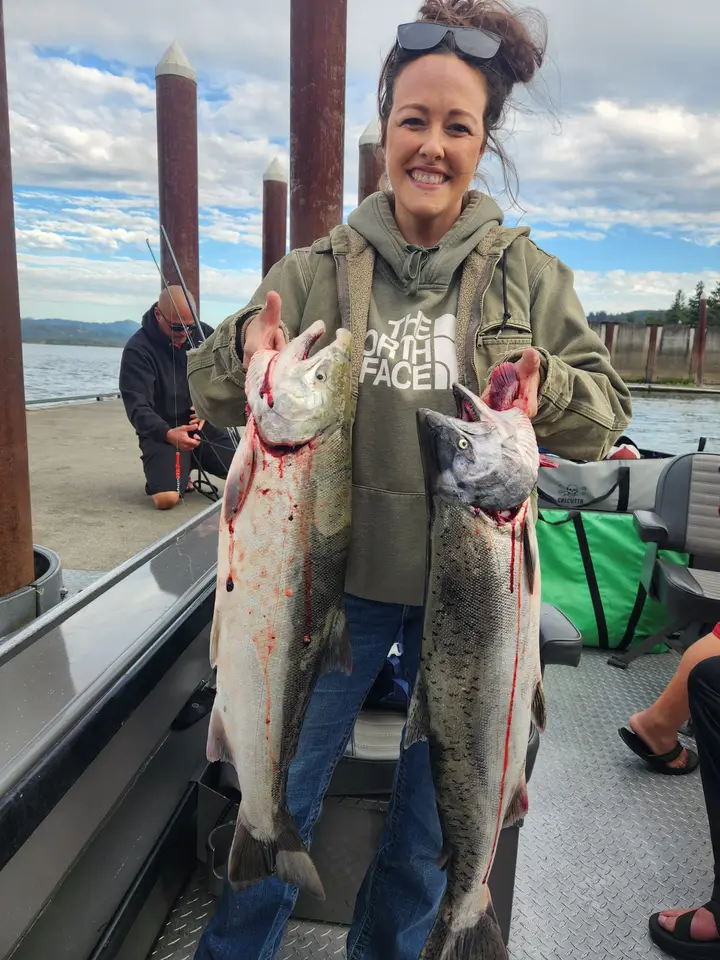 A woman holding two chinook salmon on the boat