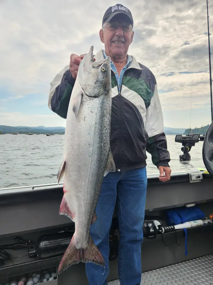 An older man in a fishing cap holding a coho salmon