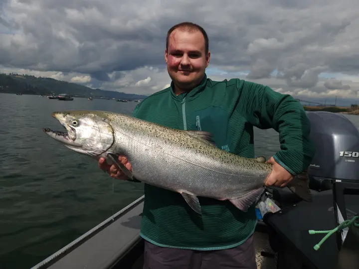 A young man in a green jacket holding a chinook salmon