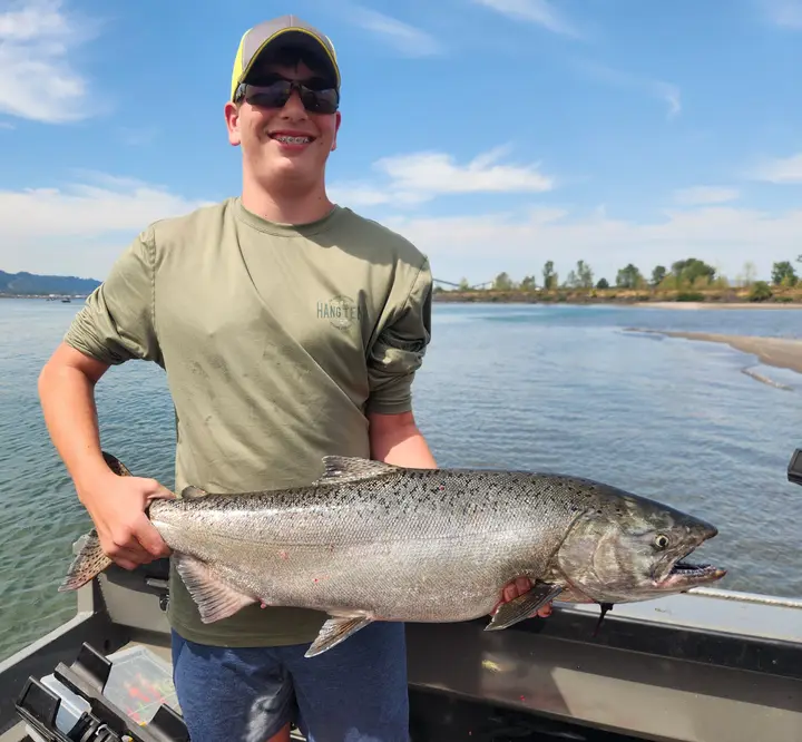 A teenage boy grinning while holding a large chinook salmon