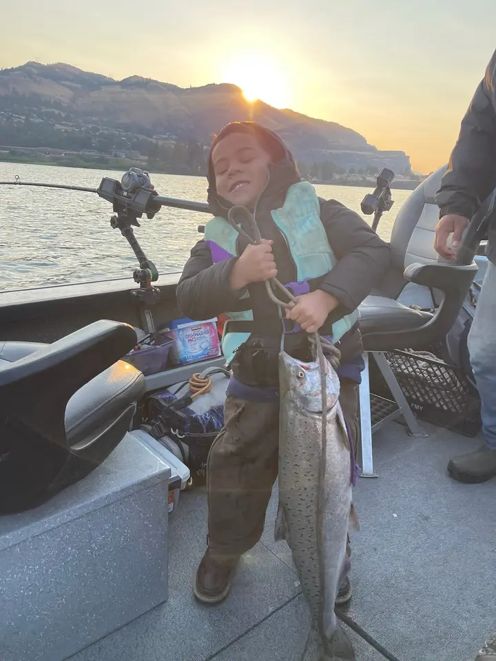 A young boy holding a chinook salmon on a rope at sunrise in the Columbia Gorge