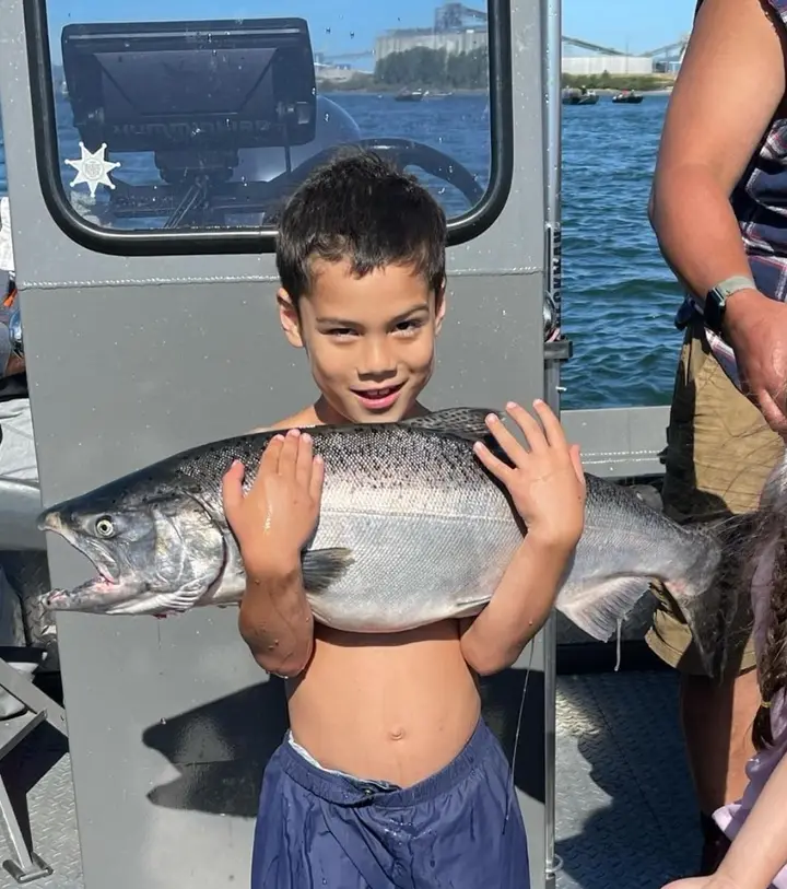 A boy holding a chinook salmon across his chest on a sunny day