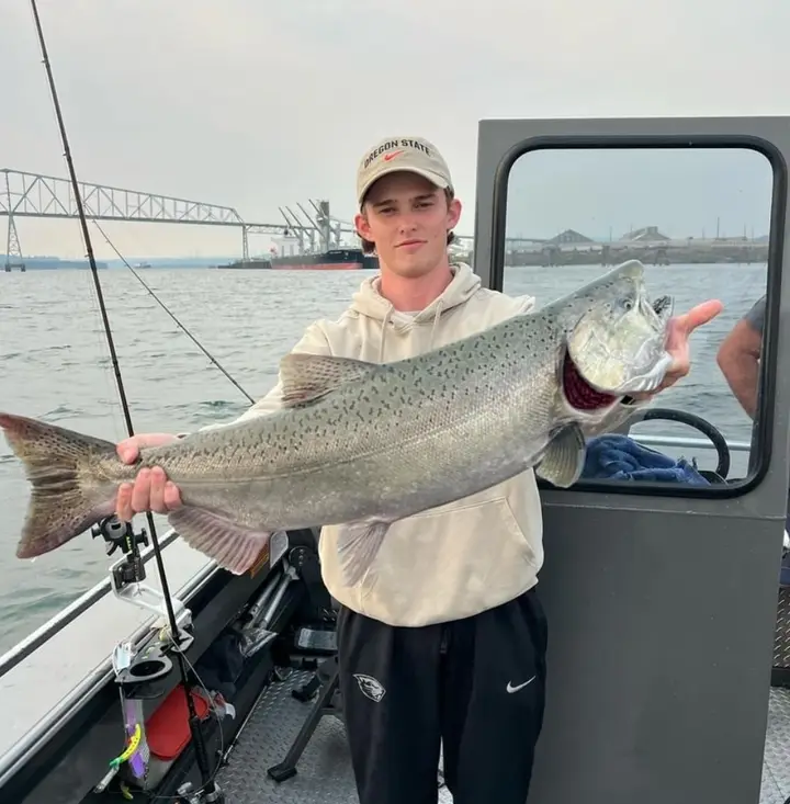A young man in an Oregon State cap holding a large chinook salmon