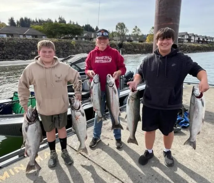 A woman and two teenage boys at the boat ramp holding six coho salmon