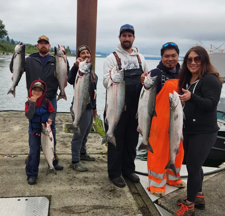A group of five adults and a boy on the dock, each holding a salmon