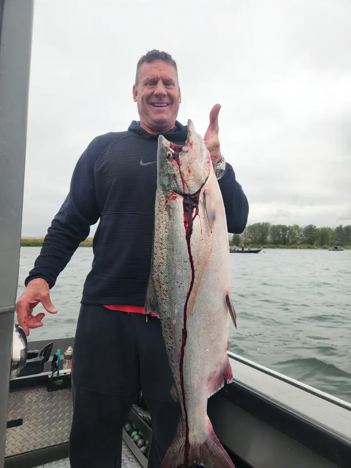 A man in a black hoodie holding a large chinook salmon