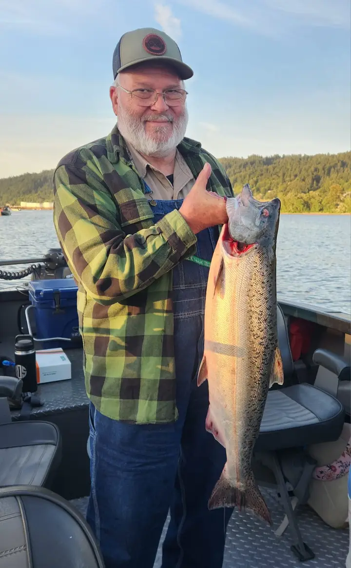 An older man in a green plaid shirt holding a chinook salmon
