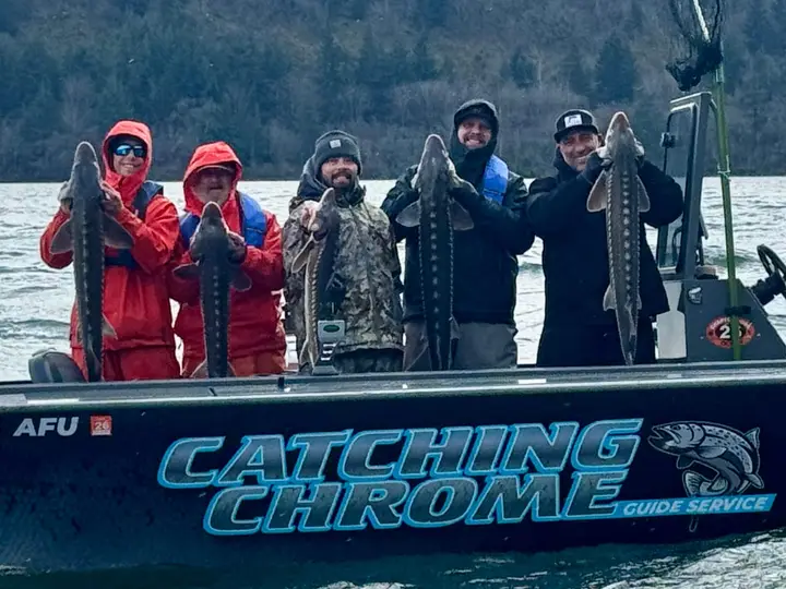 Five people aboard the Catching Chrome boat holding a large sturgeon
