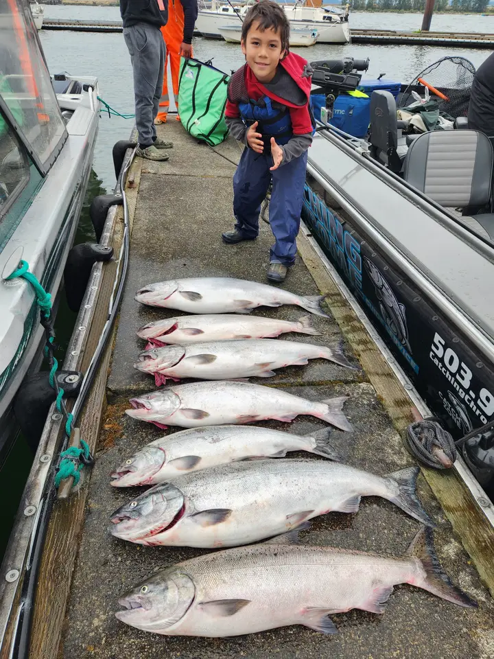 A young boy standing on the dock beside eight salmon and the Catching Chrome boat