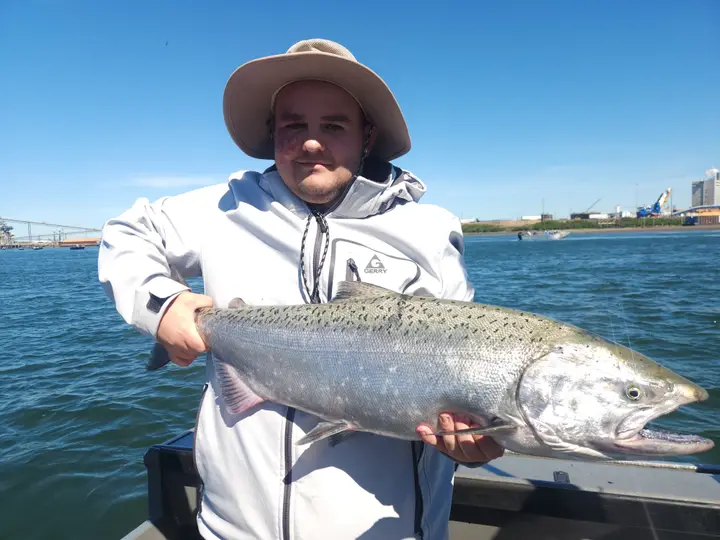 A man in a sun hat holding a chinook salmon under a blue sky