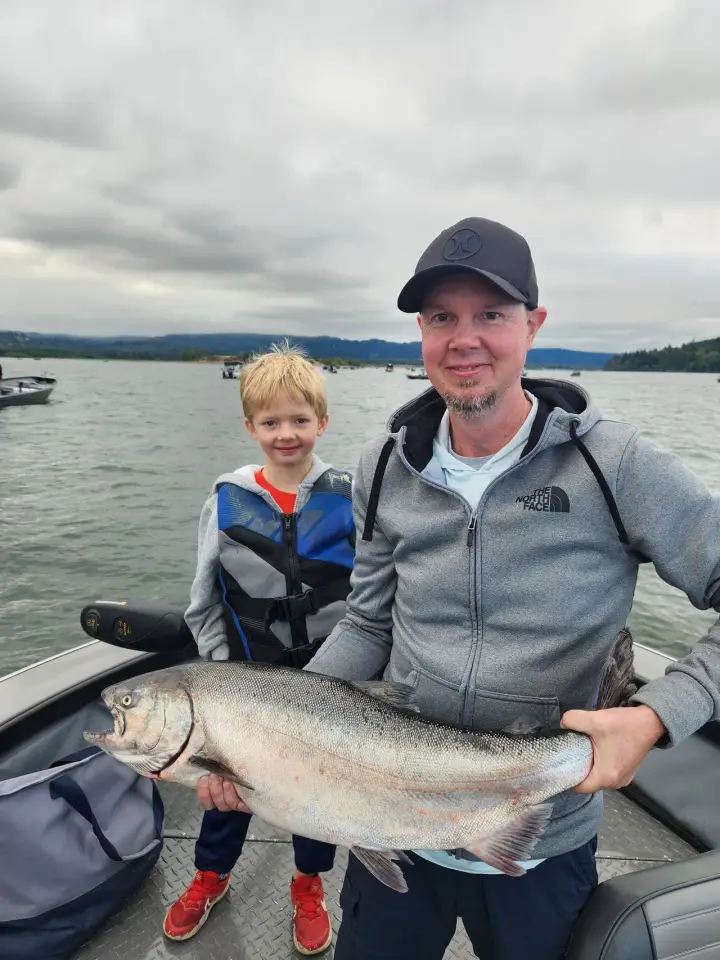 A young boy and his father holding a large coho salmon