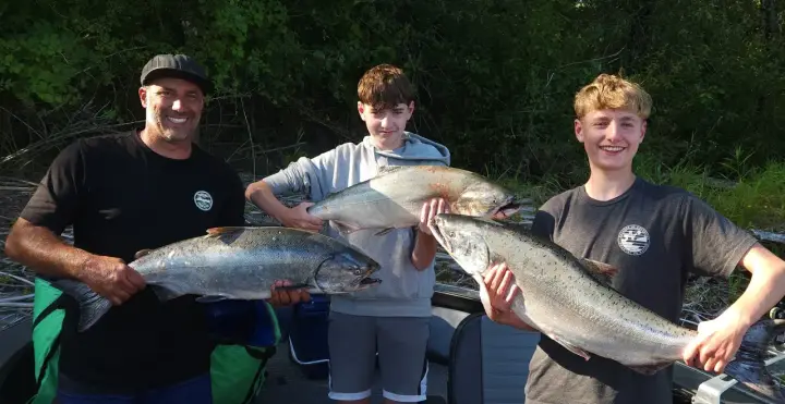 A man and two teenage boys holding three chinook salmon