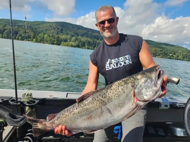 A man holding a big chinook salmon with a riverside saloon behind him